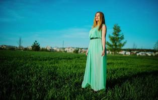 frau in einem schönen langen türkisfarbenen kleid, das auf einer wiese auf gras aufwirft. foto