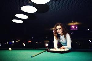 Junges lockiges Mädchen posierte in der Nähe eines Billardtisches. sexy Model im schwarzen Mini-Minirock russisches Snooker spielen. spiel und lustiges konzept. foto