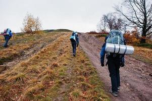 Rückansicht von drei Touristen mit Reiserucksäcken, die auf den Berg gehen foto