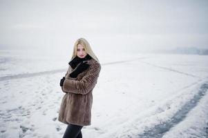 Porträt des blonden Mädchens der jungen Eleganz in einem nebligen Fluss des Pelzmantelhintergrundes auf Wintereis. foto