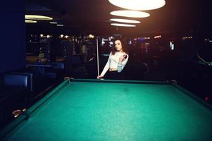 Junges lockiges Mädchen posierte in der Nähe eines Billardtisches. sexy Model im schwarzen Mini-Minirock russisches Snooker spielen. spiel und lustiges konzept. foto