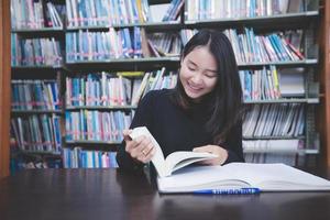 asiatische studentinnen, die bücher lesen und notizbuch in der bibliothek verwenden.