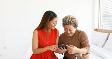 Fröhliches junges Mädchen mit einer älteren Frau, die zu Hause mit einem digitalen Tablet spielt foto