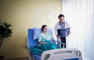 Der Arzt erklärt einer Patientin, die in einem Krankenhaus im Bett liegt, über die Röntgenergebnisse des Gehirns foto