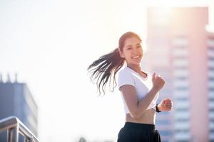 lächelnde asiatische junge Fitnesssportlerin, die in einem städtischen Gebiet läuft und sportliche Menschen trainiert, gesunde Lebensweise und Sportkonzepte foto