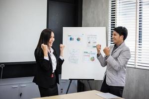 asiatischer geschäftsmann und geschäftsfrau erfolg und gewinnkonzept - glückliches team mit erhobenen händen, das den durchbruch und die errungenschaften feiert foto