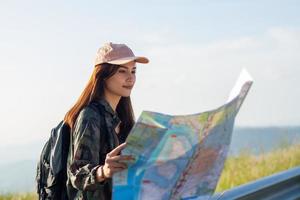 frauen asiatisch mit hellem rucksack, der eine karte betrachtet. Blick von der Rückseite des touristischen Reisenden auf den Hintergrundberg, weibliche Hände mit Smartphone, foto