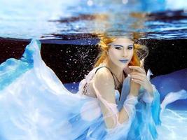 Unterwassermodeporträt der schönen blonden jungen Frau im blauen Kleid foto