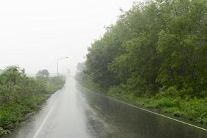 Straße vor der nassen Asphaltstraße. während der Regenzeit. Entlang des Weges liegen Kautschukplantagen und üppige Gräser. unter dem dunklen himmel in thailand. foto