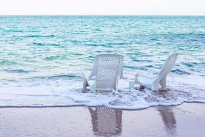 leere weiße Plastikstühle am Strand mit wunderschönen weißen Meereswellen. foto