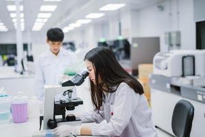 Zwei medizinische Wissenschaftler, die im medizinischen Labor arbeiten, junge Wissenschaftlerin, die sich das Mikroskop ansieht. Fokus auf junge Wissenschaftlerinnen wählen foto