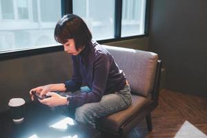 junge asiatische frau mit handy im café mit einer tasse kaffee foto