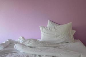 Unordentliche Decke und Kissen mit weißen Falten auf rosa Hintergrund. foto