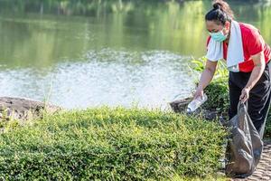 Frau räumt auf, indem sie Plastikflaschen an einem natürlichen Wasserreservoir aufhebt. konzept des schutzes der umwelt, der rettung der welt, des recyclings, der reduzierung der globalen erwärmung, des erdtages. Nahaufnahme, unscharfer Hintergrund foto