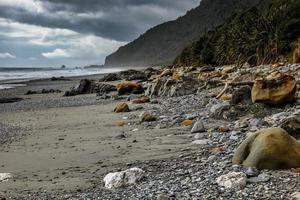 Stürmisches Wetter nähert sich einem mit Felsen übersäten Strand in Neuseeland foto