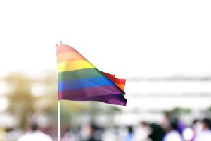 stolz regenbogen lgbt homosexuelle flagge, die in der hand hält und in der brise gegen blauen himmel geschwenkt wird. foto
