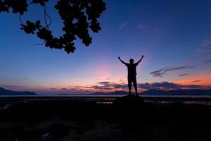 Silhouette des Mannes hob seine Hände mit Baumrahmen bei Sonnenuntergang oder Sonnenaufgang am Himmel
