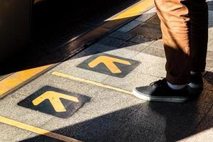 Mann steht am gelben Pfeilschild und wartet auf ein Fahrzeug der öffentlichen Verkehrsmittel. Transportkonzept. foto