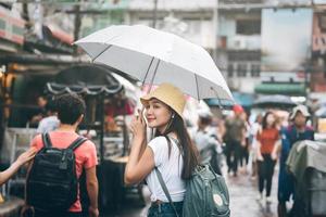 junger erwachsener asiatischer reisender hält regenschirm, wenn es in der walking street regnet. foto