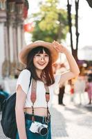 junges Mädchen mit asiatischem Einfluss, das mit Kamera und Rucksack in Bangkok reist. foto