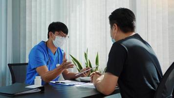 Ärzte erklären die Behandlung eines kranken Patienten in Tablettenform, während sie während des Virusausbruchs eine Maske tragen. foto