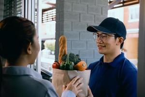 lieferung asiatischer mann, der einer asiatischen frau vor seinem haus eine papiertüte mit gemüse oder essen überreicht. foto