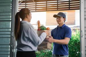 Lieferung eines asiatischen Mannes, der eine Tüte mit Lebensmitteln an eine Kundin an der Tür handhabt. foto