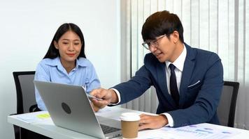 Ein asiatischer männlicher Manager bringt den Mitarbeitern an ihren Schreibtischen die Buchhaltung bei. foto