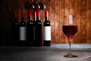Rotwein in klarem Glas, viele unscharfe Weinflaschenhintergründe platzieren ihn auf einem Zementboden mit einer Holzbrettwand. die kellerverkostung produktionskonzept.3d-rendering