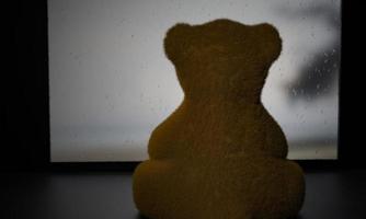 brauner teddybär sitzt und schaut während des regens mit traurigen gefühlen aus dem fenster. Regenwasser klebt an der Fensterscheibe draußen ist ein Meerblick. 3D-Rendering foto