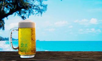 Bier vom Fass oder Craft Beer in einem hohen klaren Glas mit Bierschaum oben und es gibt Blasen im Glas. kaltes bier in einem glas, aufgestellt auf einem holztisch am strand, tagsüber das meer. 3D-Rendering