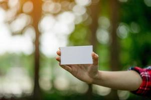 Mädchen, das eine weiße Visitenkarte hält. auf einem natürlichen grünen hintergrund und es gibt einen kopienraum. foto