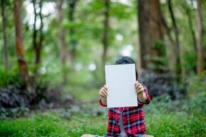 Mädchen, das A4-Papier unter dem grünen Baum hält. und es gibt einen Kopienraum. foto