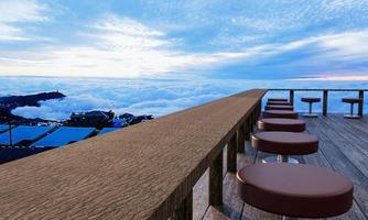 holztisch und stuhlgarnitur auf der holzterrasse des bergrestaurants im hintergrund ein nebelmeer. Nebelmeer, touristische Attraktion phu thap berk, thailand.3d-rendering foto