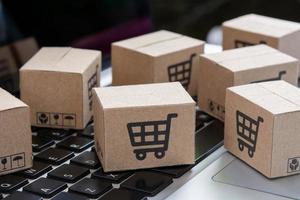 Online-Shopping - Papierkartons oder Pakete mit einem Einkaufswagen-Logo auf einer Laptop-Tastatur. Einkaufsservice im Internet und bietet Lieferung nach Hause an. foto