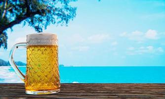 Bier vom Fass oder Craft Beer in einem hohen klaren Glas mit Bierschaum oben und es gibt Blasen im Glas. kaltes bier in einem glas, aufgestellt auf einem holztisch am strand, tagsüber das meer. 3D-Rendering foto