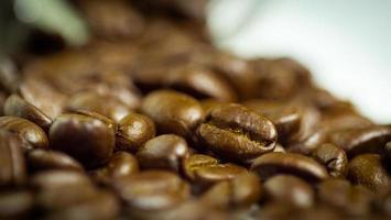 Geröstete Kaffeebohnen bereiten sich darauf vor, dass der Mahlgrad aus einer Glasflasche gegossen wird, die auf einem weißen Hintergrund liegt, um frischen Kaffee zuzubereiten oder in eine Espressomaschine oder Moka-Kanne zu gehen foto