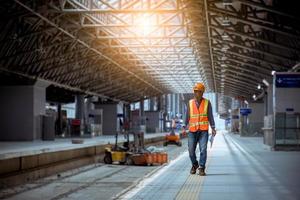 Ingenieur Eisenbahn unter Überprüfung des Bauprozesses Zugprüfung und Überprüfung der Eisenbahnarbeiten am Bahnhof mit Funkkommunikation. Ingenieur mit Sicherheitsuniform und Schutzhelm bei der Arbeit. foto