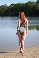 Rückansicht einer jungen Frau mit khakifarbenem Badeanzug, die am Strand am Badesee steht foto