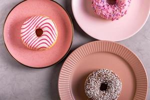 Drei glasierte Donuts liegen auf hohen rosa Tellern foto