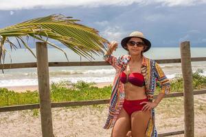 Dame in Badebekleidung, die sich an einen Holzzaun nahe dem Strand in Caraiva Bahia, Brasilien, lehnt foto