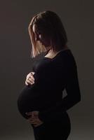 stilvolle schöne schwangere frau in einem schwarzen kleid hält ihre hände auf ihrem bauch.