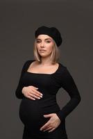 stilvolle schöne schwangere frau in einem schwarzen kleid hält ihre hände auf ihrem bauch. foto