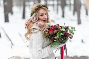 ein junges Mädchen slawischen Aussehens mit einem Kranz aus Wildblumen. Schöne blonde Braut hält einen Blumenstrauß im Winterhintergrund. foto