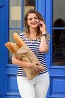 junge schöne frau, die mit einem baguette in ihren händen auf den straßen von frankreich posiert. foto