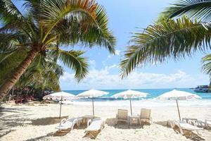 Sommerurlaub Natur Reisen schöne Sommerlandschaft mit Stuhl Sonnenschirm auf Sand - tropischer Urlaub Kokosnussblatt Palme am Strand mit Sonnenlicht auf blauem Himmel Meer und Ozean Hintergrund foto