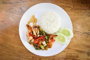 Gebratene Meeresfrüchte, Tintenfisch, Garnelen, Garnelen mit heiligem Basilikum und Reis thailändisches Essen, würziges frittiertes Rezept mit Gurke und Chili foto