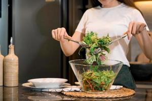 asiatische hausfrau, die frisches gemüse zubereitet, um salat zu hause küchentheke zuzubereiten. foto