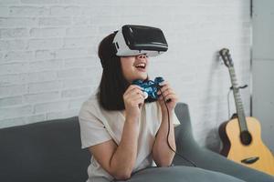 asiatische frau spielt vr-spiel zur unterhaltung zu hause, asiatische frau freut sich im haus im urlaub. glückliche frau, die metaverse vr-technologiekonzept spielt. foto