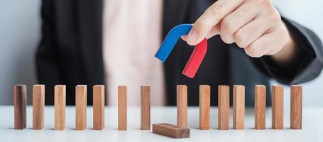 Geschäftsfrau hält Magnet in der Hand und zieht Mann-Holzfigur aus dem Massenblock. Business, Personalmanagement, Rekrutierung, Teamarbeit, Strategie, toxische Menschen und Führungskonzepte foto